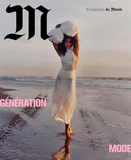 Magazine cover shot of a barefoot adult woman standing on a beach wearing a long white dress, holding white puffy objects above her head.