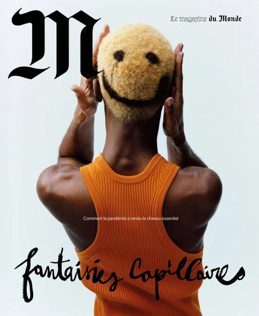 Magazine cover featuring an adult male with a smiley face haircut, wearing an orange tank top against a white background.