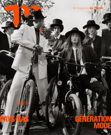 Group of models in tailored suits and top hats posing with vintage bicycles on a city street in Paris