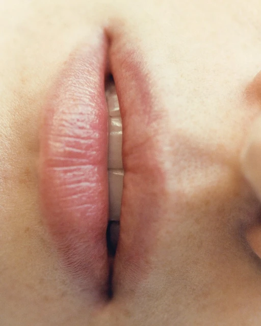 Close-up of an adult female's open mouth with visible white teeth and pink lips, presented in a high-key, eye-level shot.
