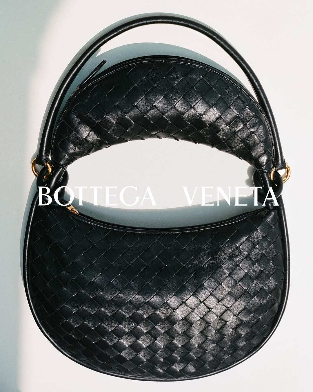 Close-up of a black Bottega Veneta woven leather handbag with a rounded shape and handle, set against a neutral background.