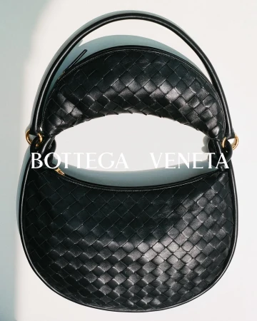Close-up of a black Bottega Veneta woven leather handbag with a rounded shape and handle, set against a neutral background.