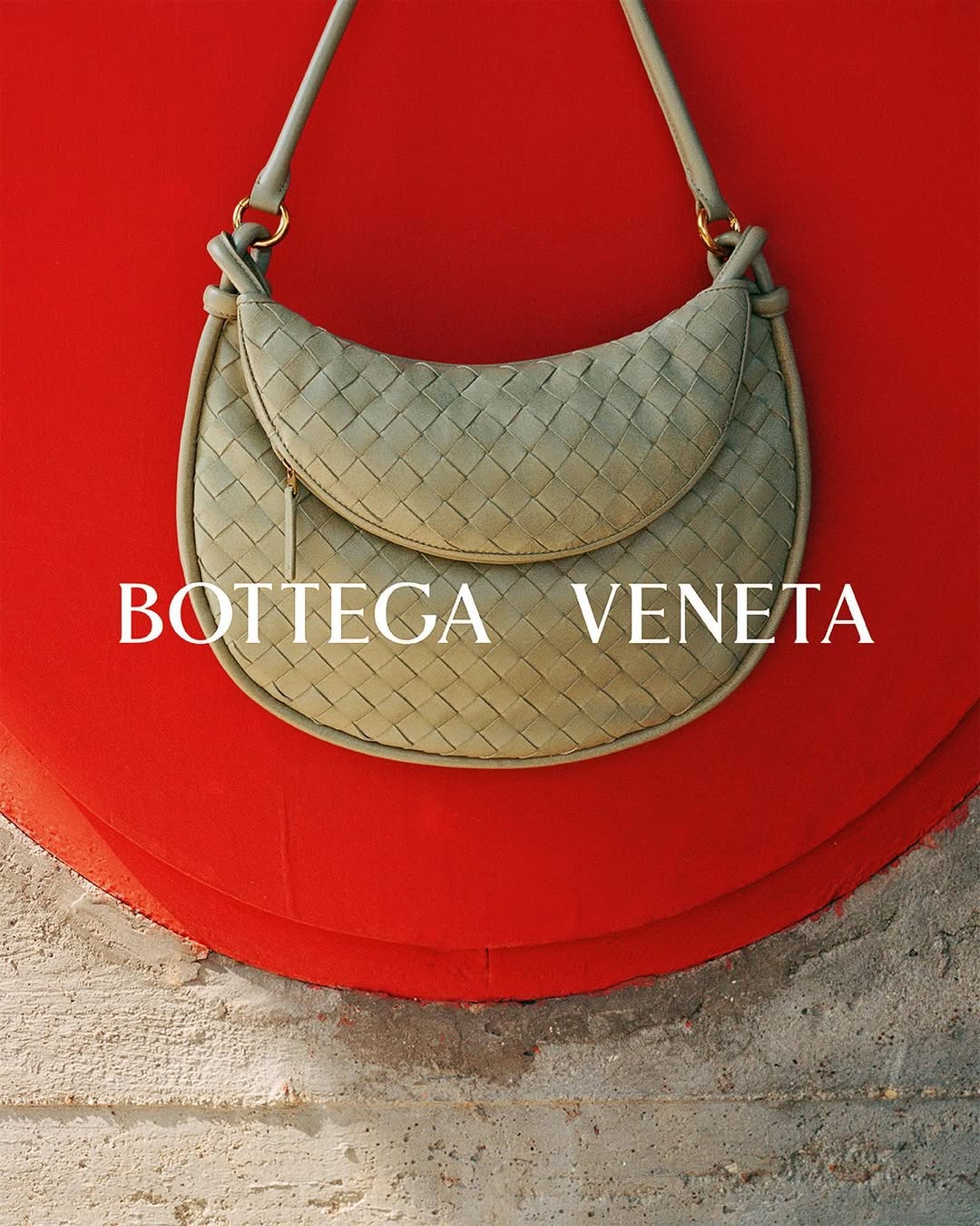 Bottega Veneta woven light green hobo bag with shoulder strap, displayed against red background and textured neutral surface.