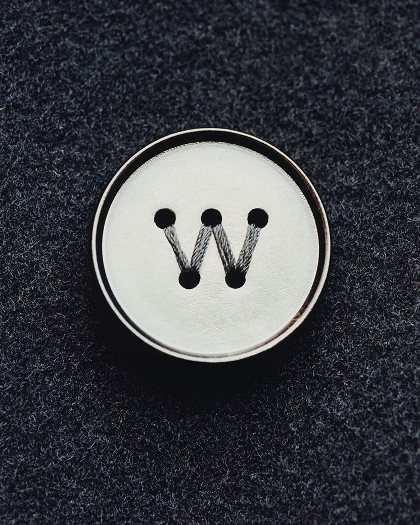 Close-up studio shot of a white button with a black letter W sewn on dark gray fabric, showcasing fashion and design elements.