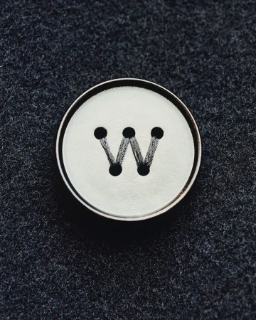 Close-up studio shot of a white button with a black letter W sewn on dark gray fabric, showcasing fashion and design elements.