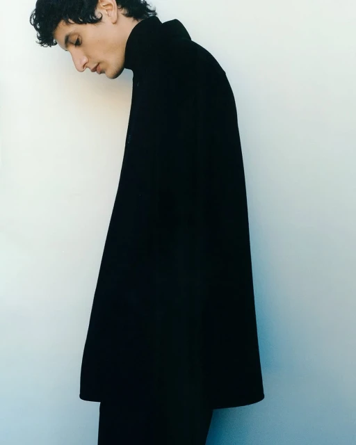 Profile portrait of an adult male model wearing a black turtleneck sweater against a white backdrop, minimalist fashion and studio lighting.
