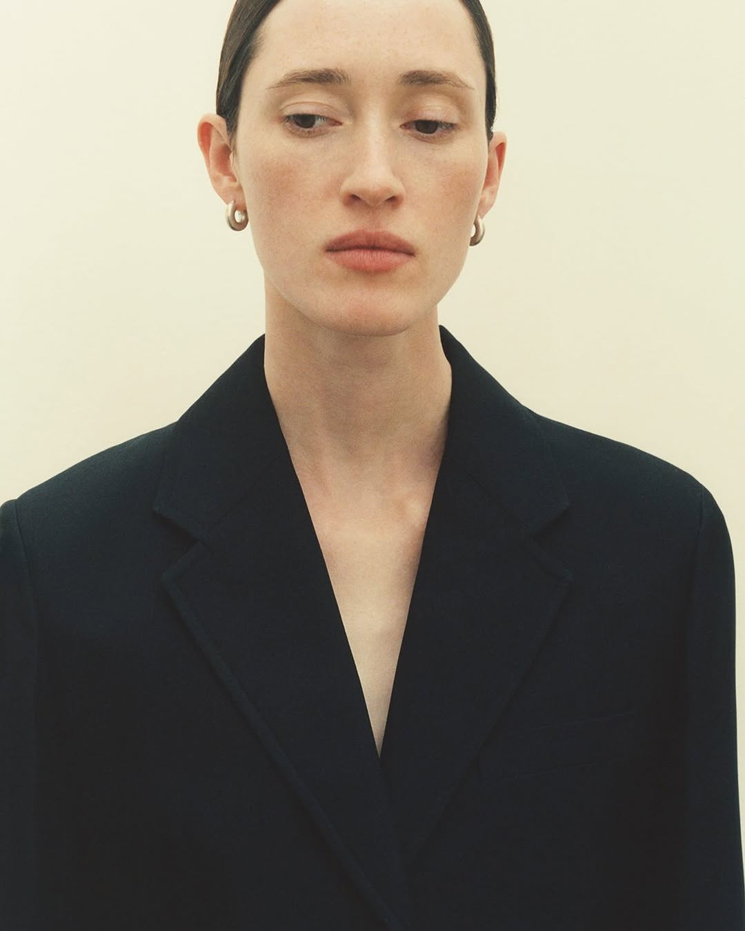 Portrait of a woman wearing a dark blazer and small hoop earrings against a neutral background