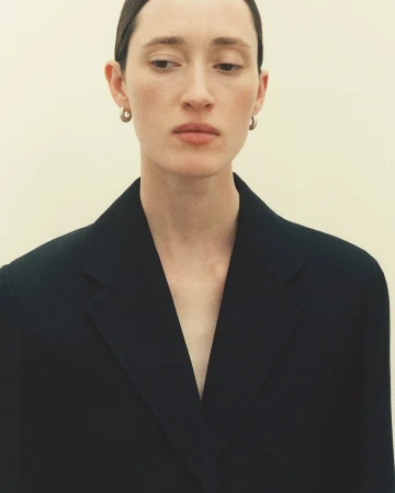 Portrait of a woman wearing a dark blazer and small hoop earrings against a neutral background