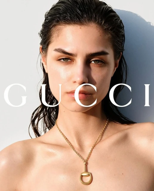 Close-up fashion portrait of a young adult woman with dark hair, wearing a gold necklace, bright studio lighting, neutral white background.