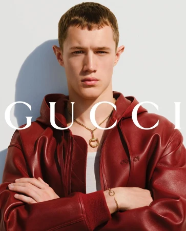 Close-up of an adult male wearing a red hooded jacket, necklace, and bracelet against a bright white background with faint shadow.