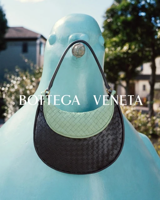 Bottega Veneta handbag on a light blue sculpture in an outdoor setting, featuring braided texture and a unique color combination.