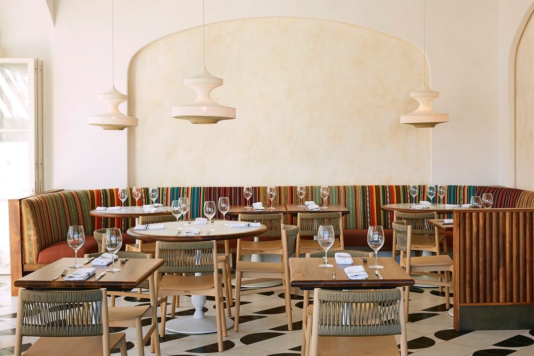 Bright and inviting restaurant interior featuring dining tables set with glassware, patterned flooring, and modern pendant lighting.