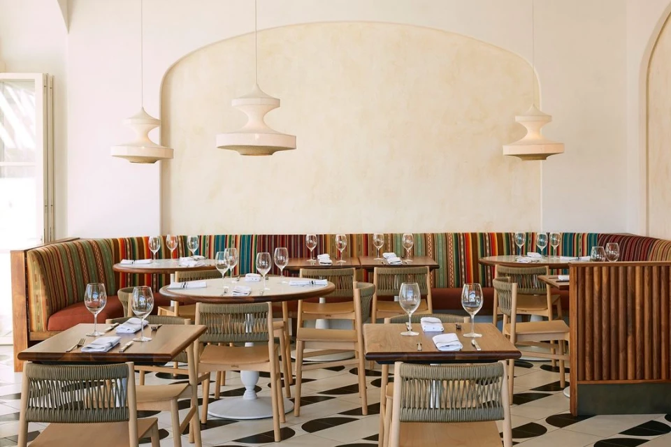 Bright and inviting restaurant interior featuring dining tables set with glassware, patterned flooring, and modern pendant lighting.