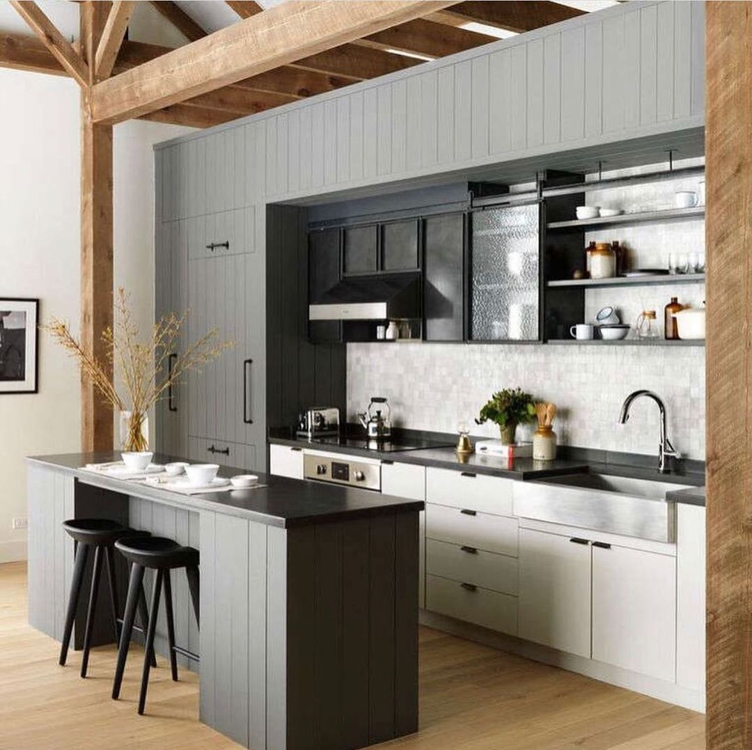 Contemporary kitchen with gray cabinets, black countertops, wooden floors, and a central island with black stools.