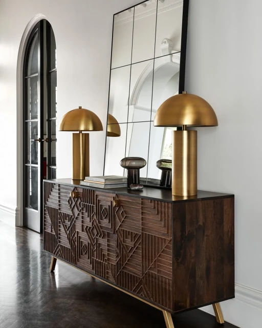 Interior design featuring a dark wood console table with gold accents, topped with gold dome lamps, against a mirrored wall.
