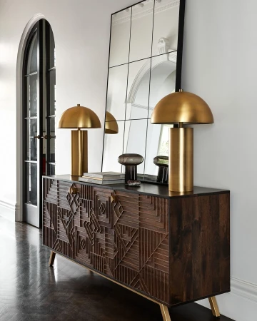 Interior design featuring a dark wood console table with gold accents, topped with gold dome lamps, against a mirrored wall.