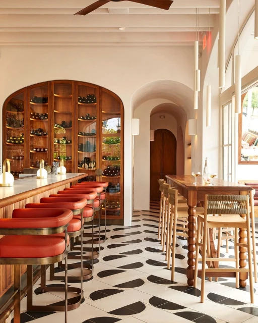 Interior view of a restaurant with a bar featuring red cushioned stools, a wine rack, and a black and white patterned floor.