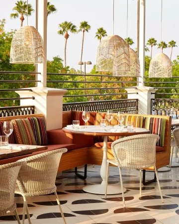 Outdoor restaurant seating area with wicker chairs, tables set for dining, and overhead lighting, capturing a warm, inviting atmosphere.