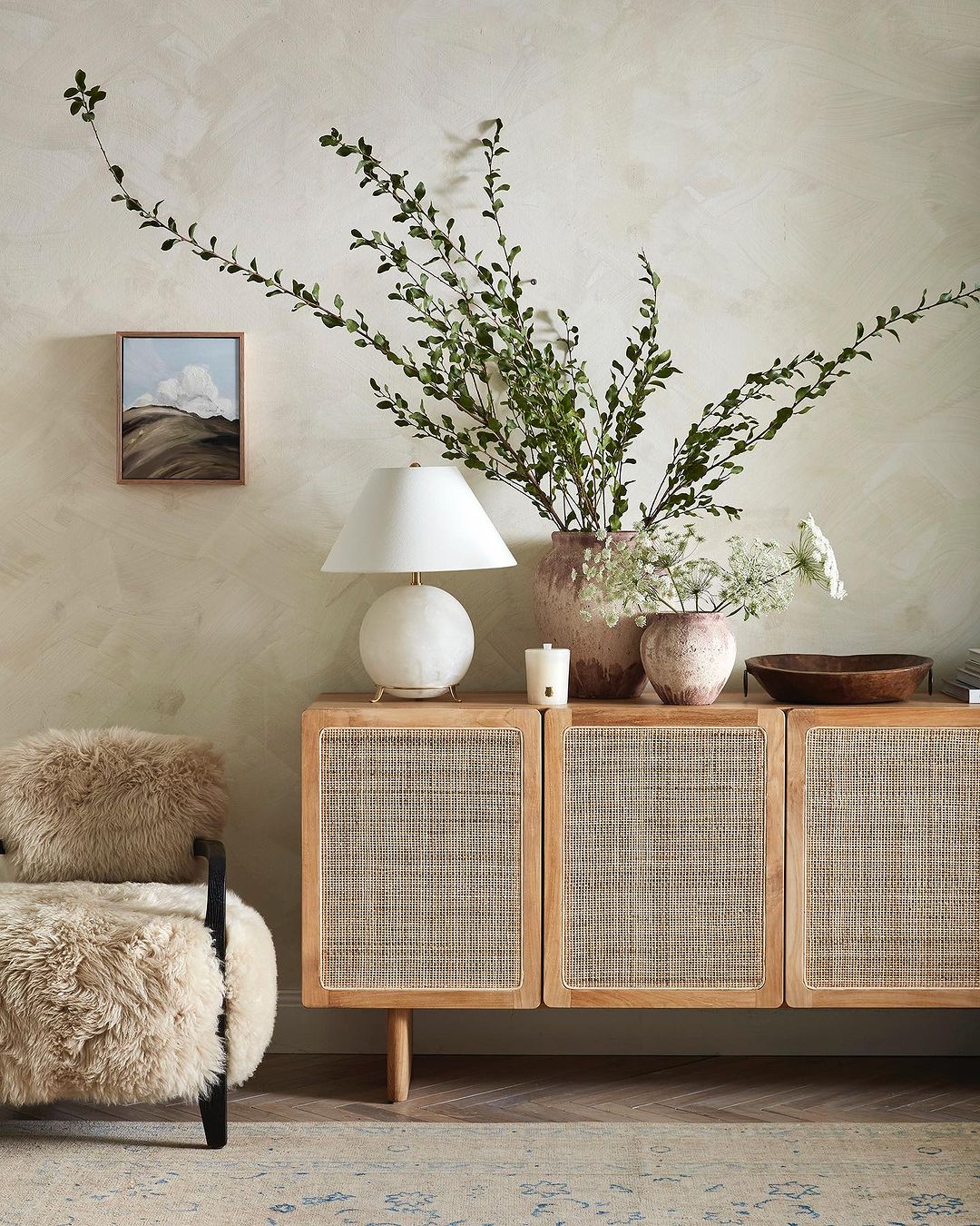 Living room interior featuring a wood cabinet with woven doors, a spherical table lamp, and a minimalist painting on a textured wall.
