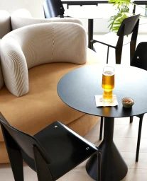 Tall glass of beer and a small bowl of nuts on a black round table inside a contemporary cafe by Jonny Valiant