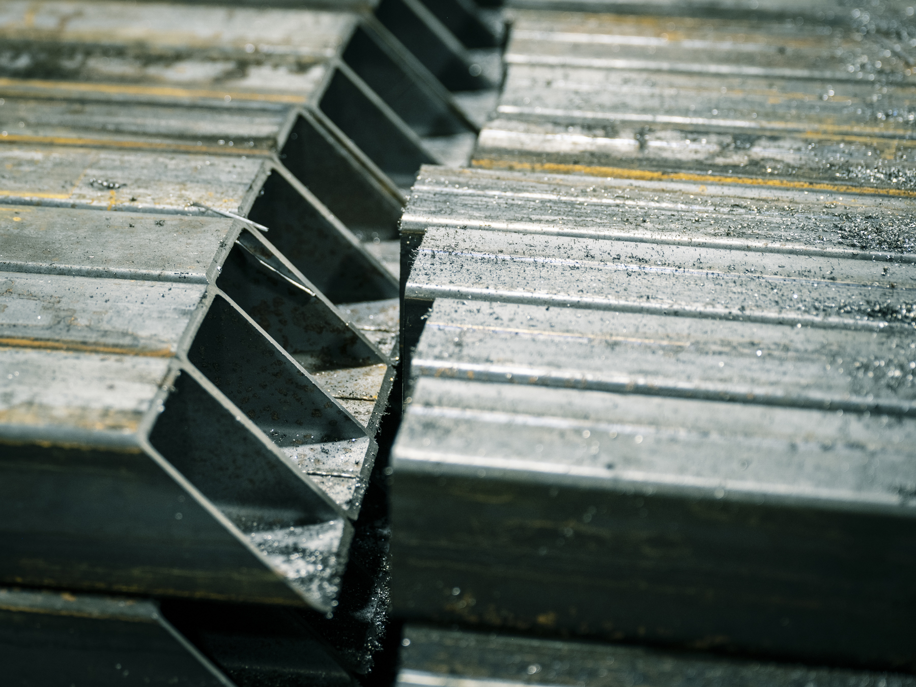 Close-up view of stacked, gray, square metal tubes. The repeating pattern shows the metal's texture and construction material.