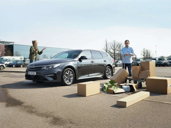 Grey Kia station wagon parked in a parking lot with a woman and a man standing nearby with moving boxes and a shopping cart.