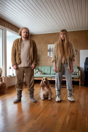 Indoor portrait of a reddish-haired man and a reddish-haired woman standing next to a Cocker Spaniel dog on a wooden floor.