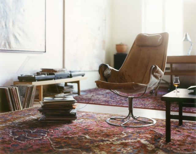 A vintage leather chair sits on a patterned rug in a living room with a record player and vinyl records. Natural light illuminates the room.