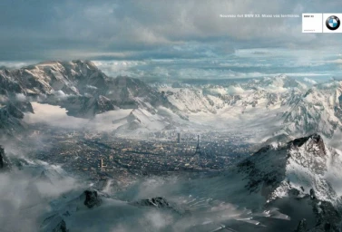 Surreal digital illustration by Jean-Marie Vives showing a sprawling city nestled in a vast snow-capped mountain range under a cloudy sky.