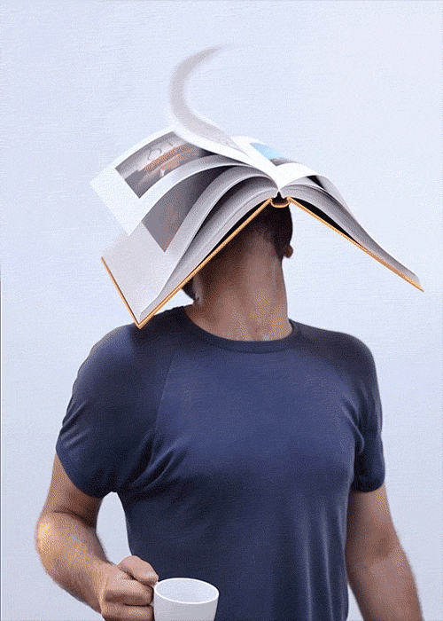 Adult male balancing an open book on his head, holding a white coffee cup in his hand against a clean white background.