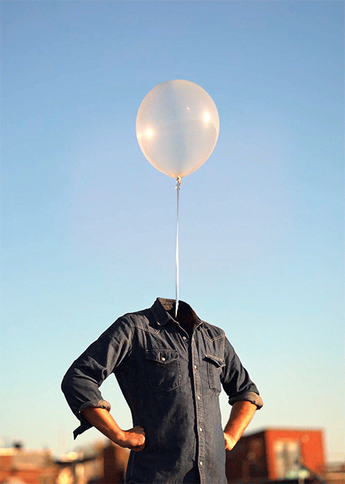 Surreal outdoor image: a denim shirt with arms akimbo stands headless with a balloon floating above the neck against a clear sky.