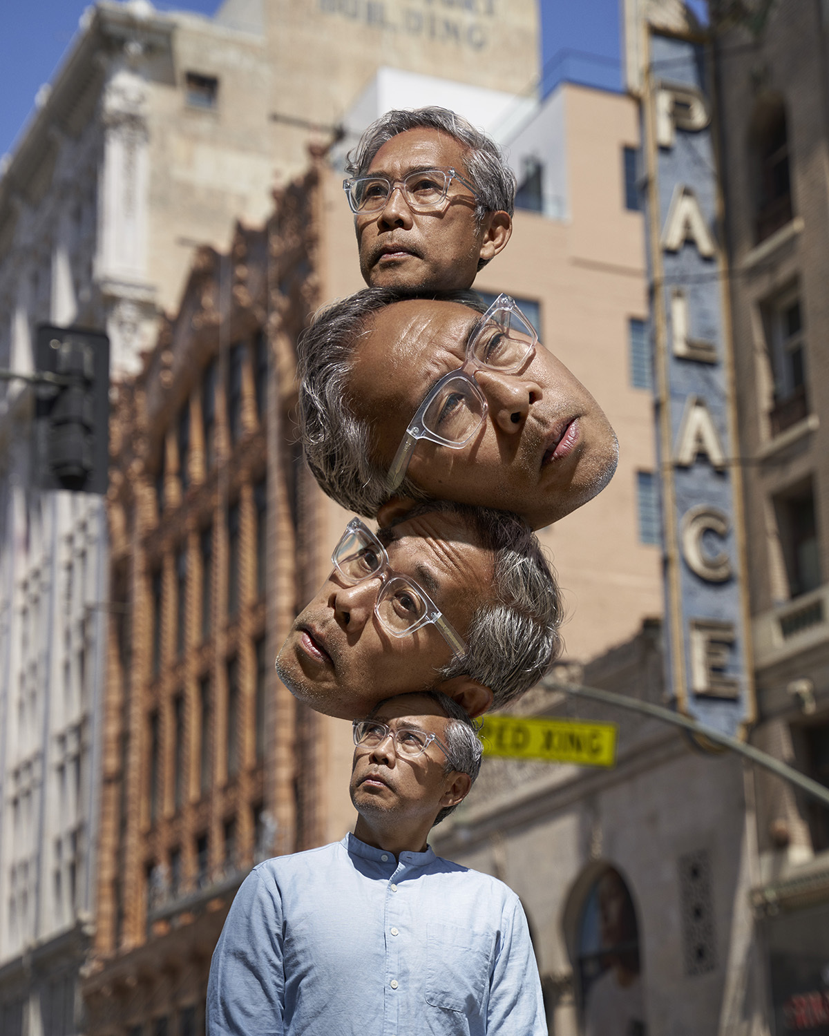 Digitally altered image of a man with three additional disembodied heads stacked above him on a city street with vintage buildings.