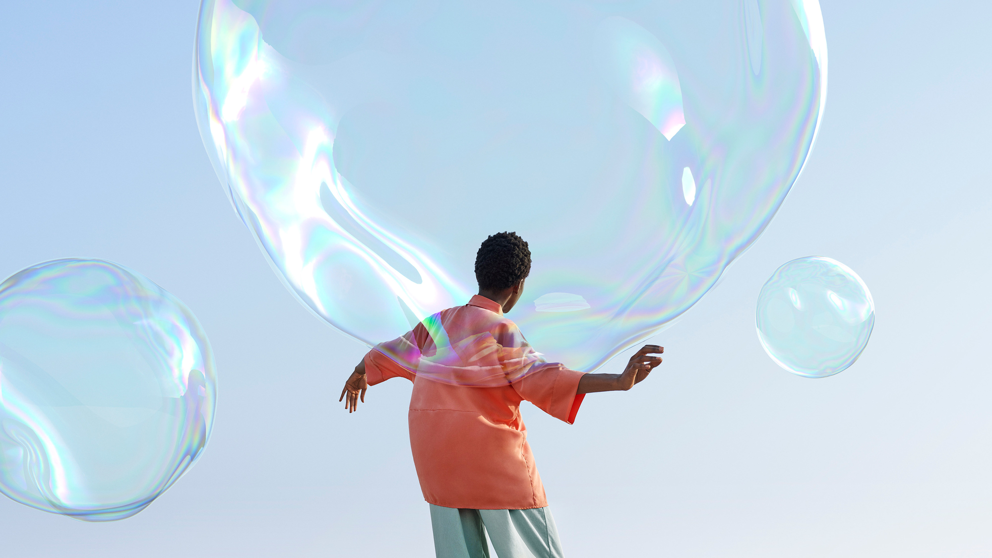 Woman in peach shirt poses with large soap bubbles against a clear sky in an outdoor setting, creating a light and whimsical scene.