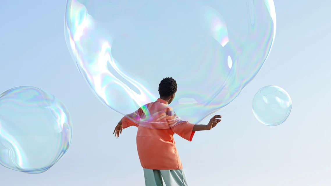 Woman in peach shirt poses with large soap bubbles against a clear sky in an outdoor setting, creating a light and whimsical scene.