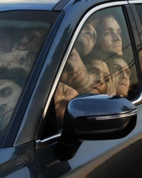Multiple faces pressed against the car window and windshield of a dark vehicle, captured in a surreal photographic portrait.