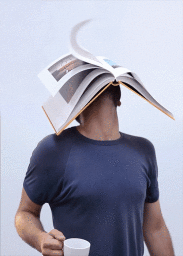 Man wearing an open book instead of a head, holding a white mug against a plain background