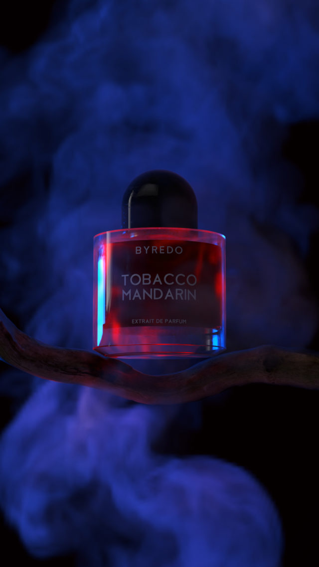 Byredo Tobacco Mandarin perfume bottle on branch, smoke effect background, studio shot for beauty and fragrance advertising.