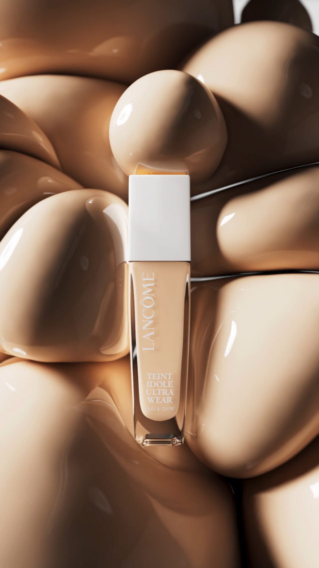 Lancôme Teint Idole Ultra Wear foundation bottle on a bed of tan, glossy cosmetic gel in a beauty and cosmetics still life.