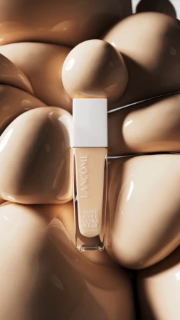 Lancôme Teint Idole Ultra Wear foundation bottle on a bed of tan, glossy cosmetic gel in a beauty and cosmetics still life.