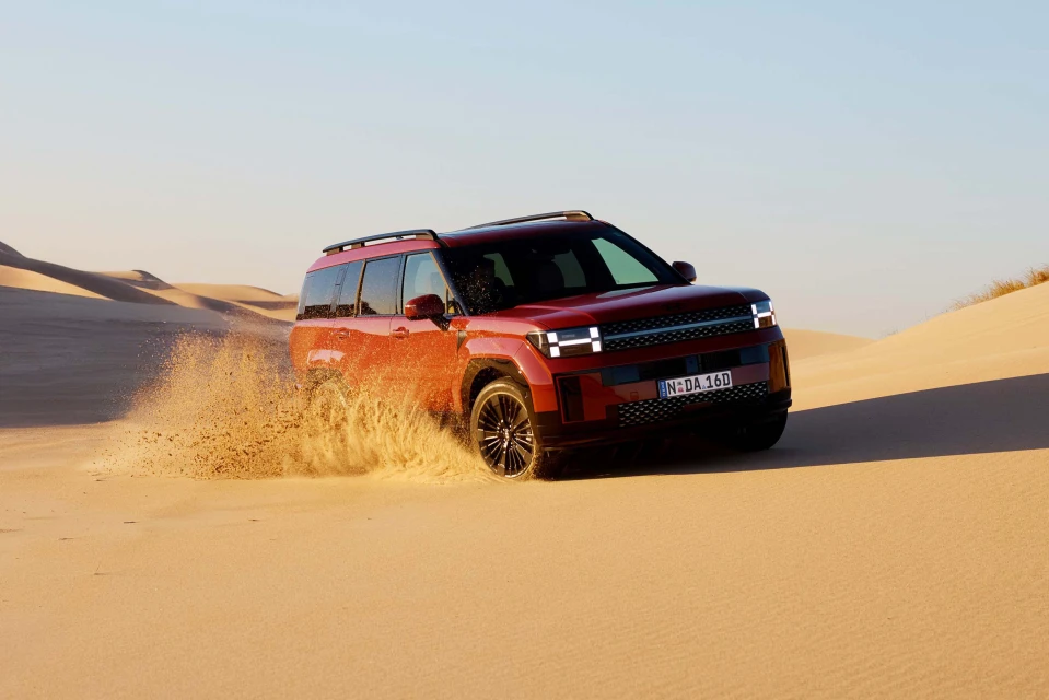 Red SUV driving through sand dunes in desert landscape. Automotive photography featuring off-road vehicle in outdoor environment.