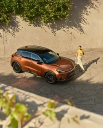 High-angle view of a copper crossover car parked on a stone paved courtyard with a woman walking beside it.