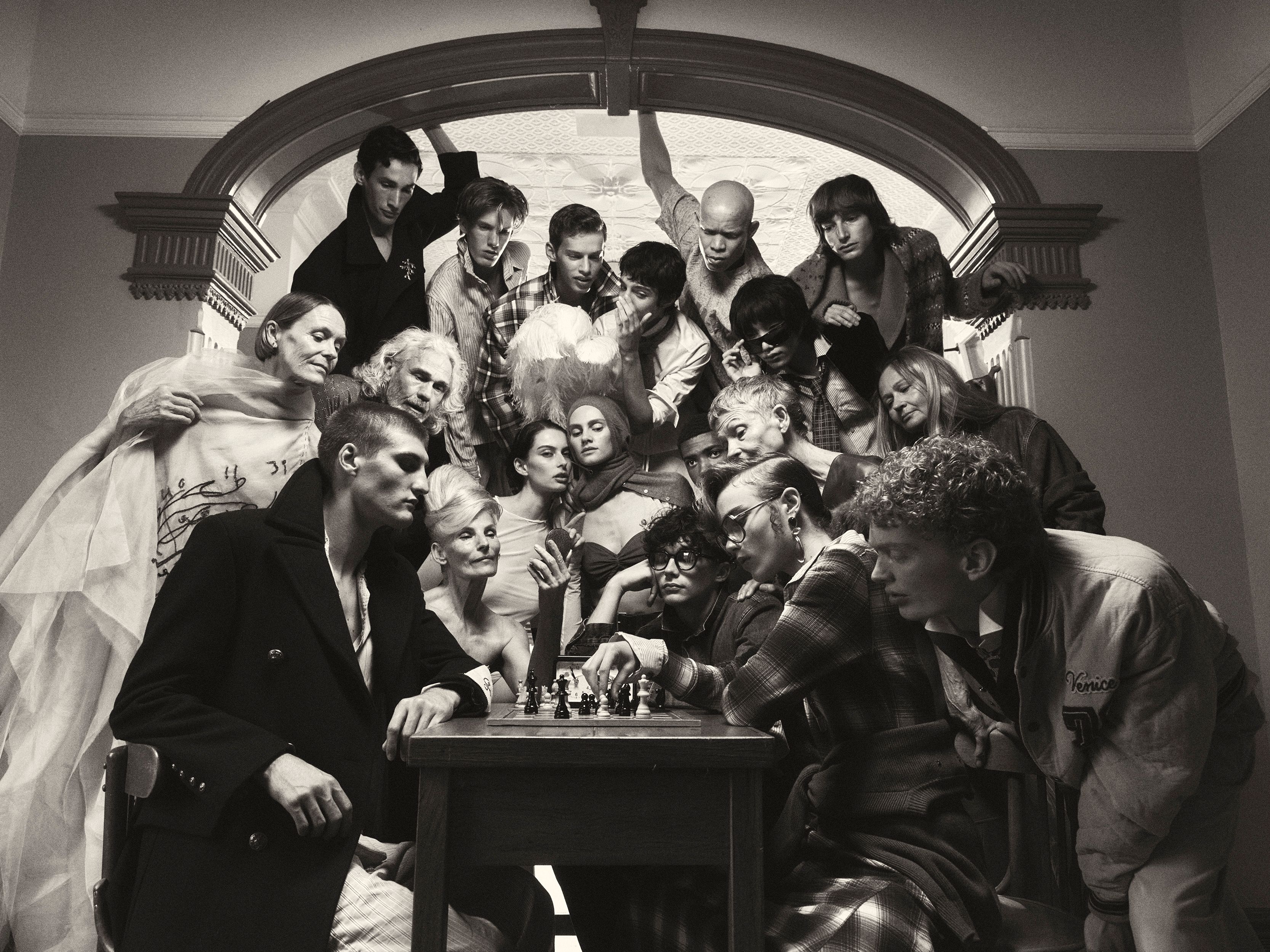 Monochromatic shot of a large group of people gathered around a chessboard, creating a sense of mystery and anticipation in an indoor setting.