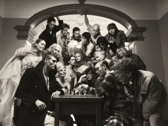 Monochrome group portrait of diverse models gathered around a table playing chess beneath an arched doorway, photographed by Adrian Price