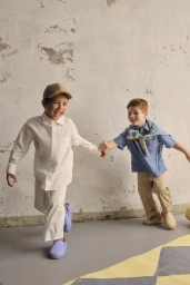 Two young boys holding hands and laughing while walking against a distressed wall and painted floor background
