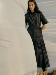 Model wearing a dark short-sleeve midi shirt dress leaning against a large white textile structure outdoors
