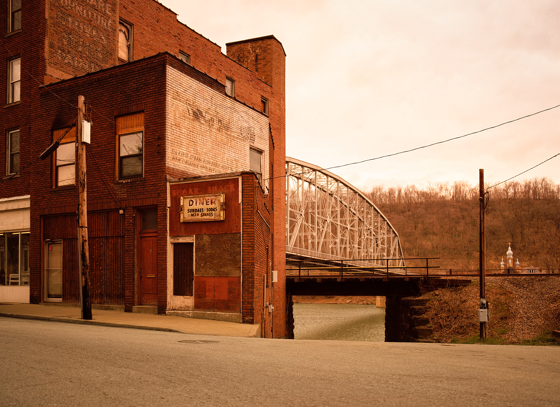 Vintage brick building with hand-painted signage and an arched metal bridge in the background under a hazy, soft-light sky.