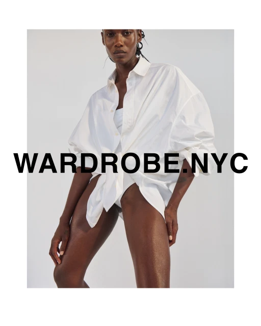 Studio shot of a tan-skinned adult woman wearing a large white collared shirt. The shirt is unbuttoned and tied at the waist.