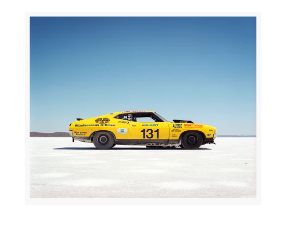 Yellow race car with number 131 parked on a salt flat against a clear blue sky, capturing the essence of speed and automotive design.
