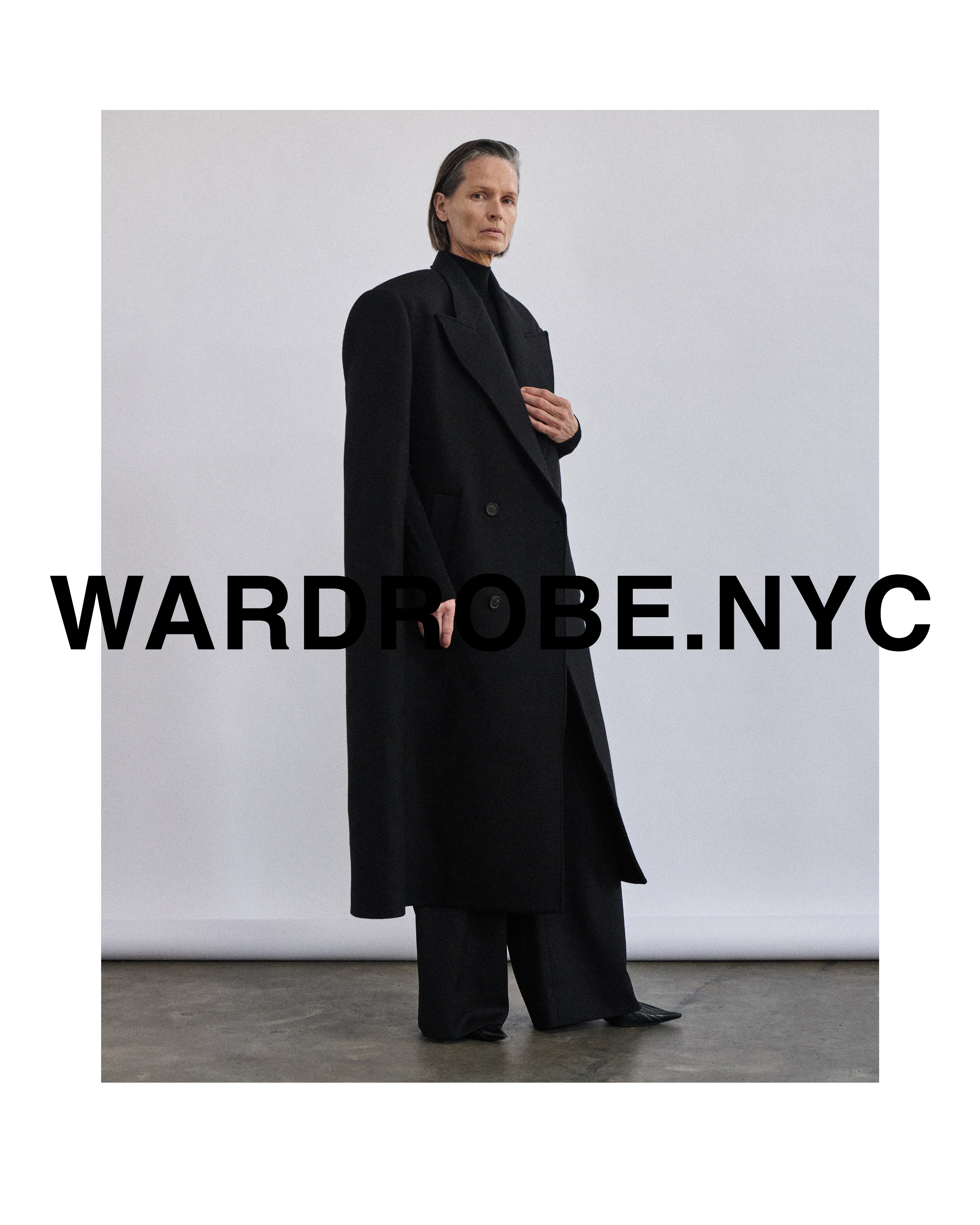 Elegant adult poses in a black double-breasted coat and wide-leg trousers against a neutral backdrop, showcasing a modern fashion silhouette.