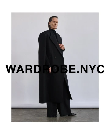 Model in long black wool coat and trousers standing against a white seamless backdrop with overlaid text